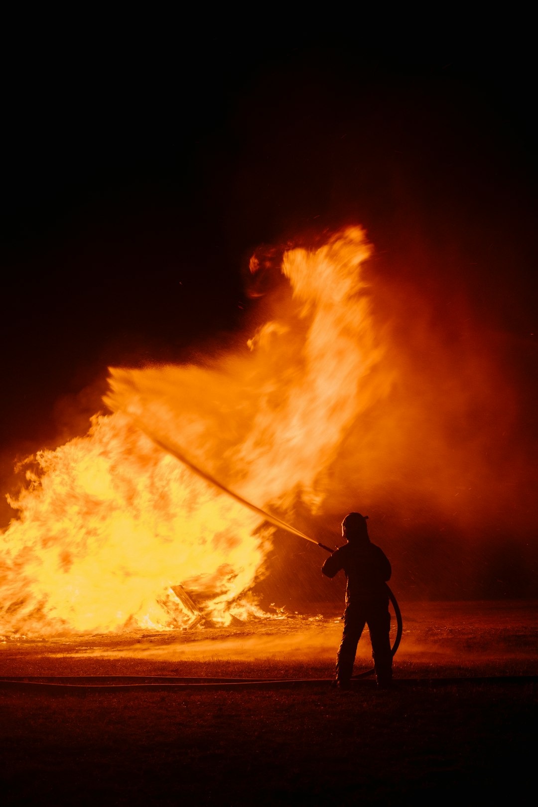 A man holding a fire hose in front of a large fire